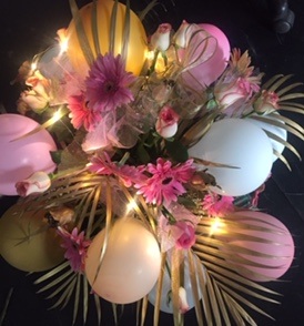 6 Pink Gold and White balloons placed in between gold leaves and 20 pink roses and gerberas and LED lights