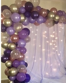 Balloon arch with shades of purple gold pink balloons and lights and leaves