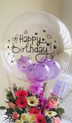 Clear Balloon stuffed with balloons and happy birthday print with basket of gerberas